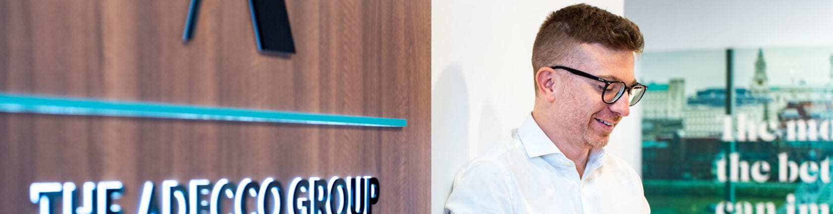 A smiling man reading documents near The Adecco Group logo, representing investor relations.