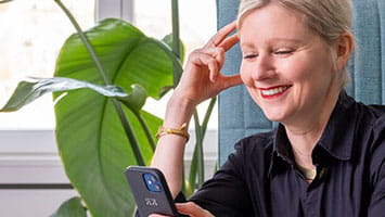 Woman smiling at her phone in a bright space with plants, representing sustainability contacts. Woman smiling at her phone in a bright space with plants, representing sustainability contacts.