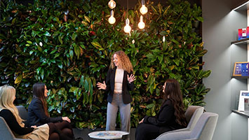 A woman presents to three colleagues in front of a green plant wall, symbolizing ethical collaboration and integrity. A woman presents to three colleagues in front of a green plant wall, symbolizing ethical collaboration and integrity.